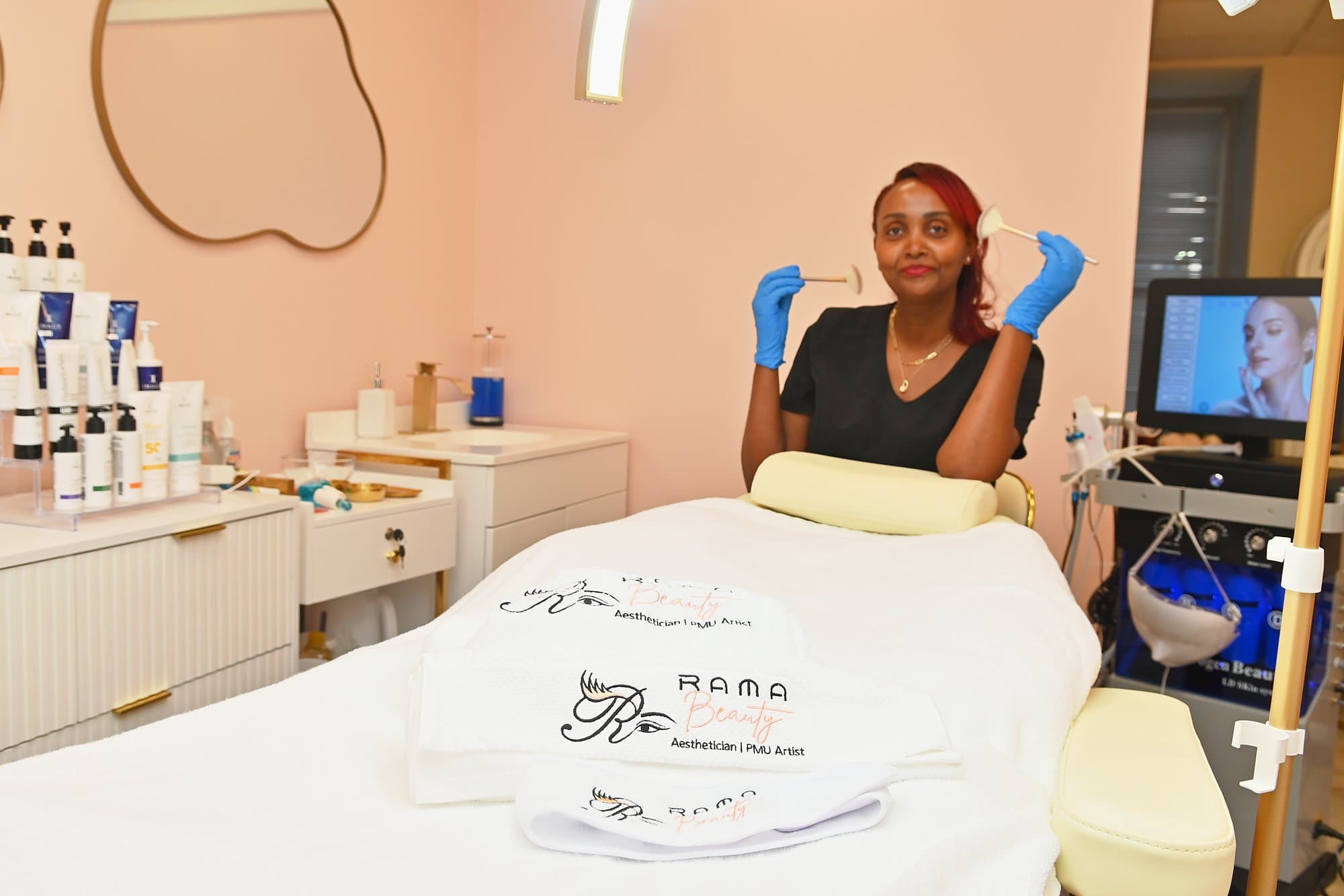 Rahwa in gloves holding fan brushes behind a treatment bed laid with Rama Beauty towels