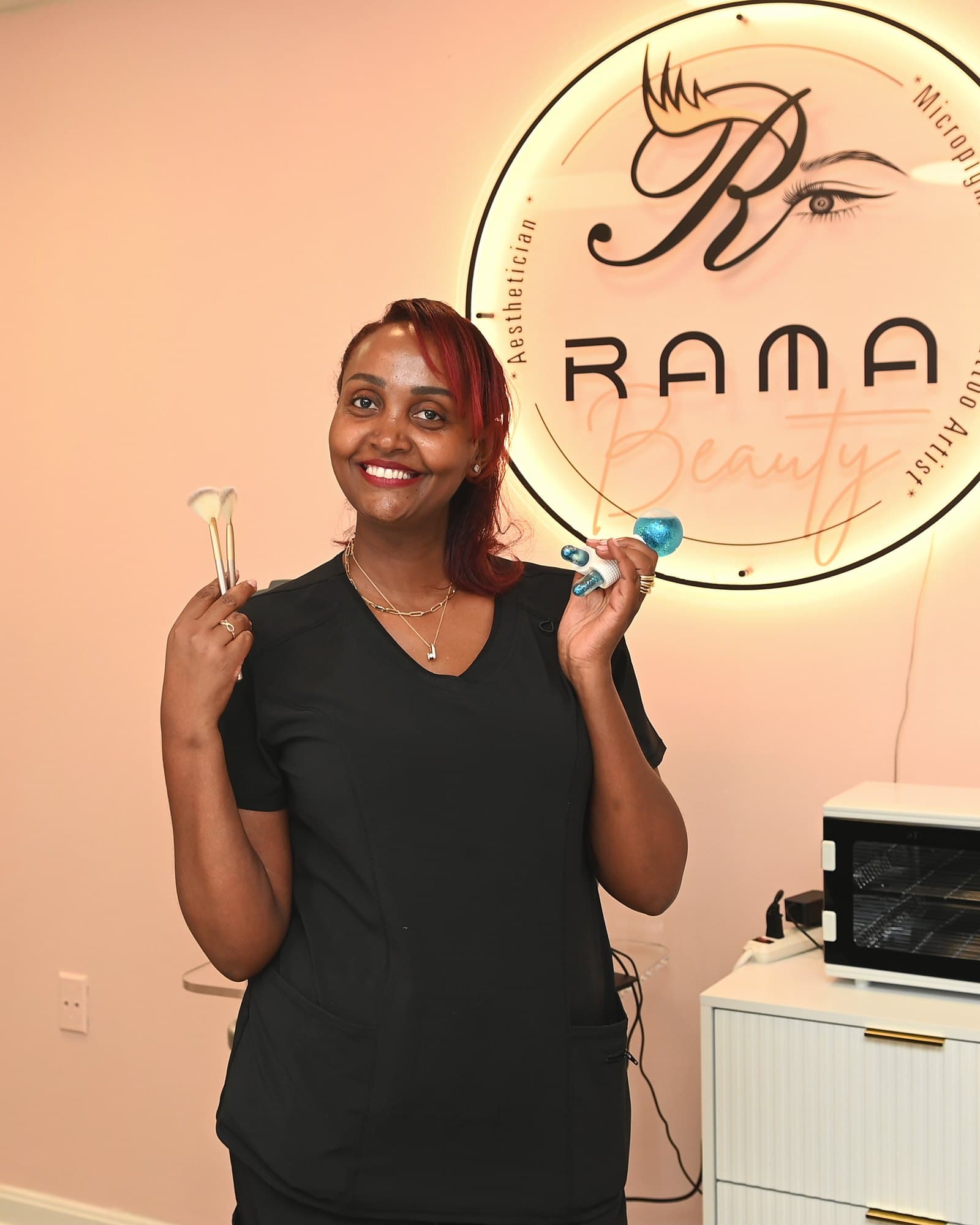 Rahwa Tameru holding a fan brush and cooling facial globes beside the lit Rama Beauty sign
